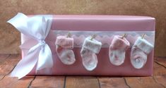 baby booties are hanging from a pink gift box with white ribbon and bows on it