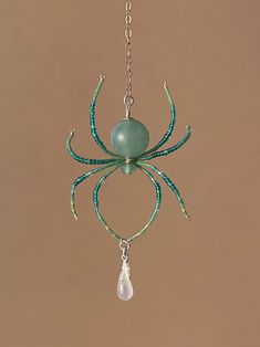 a green beaded spider hanging from a chain with a pearl drop on it's end