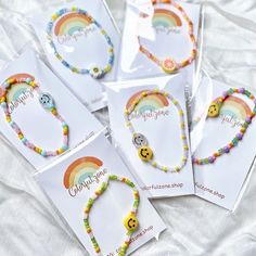 four bracelets with smiley faces and rainbow beads are on a white sheet, next to some cards that say celebrate and smile