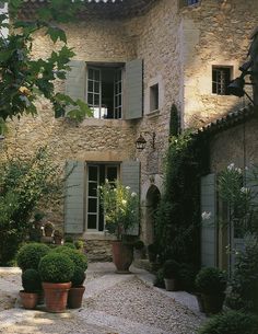 an old stone building with green shutters and potted plants in the front yard