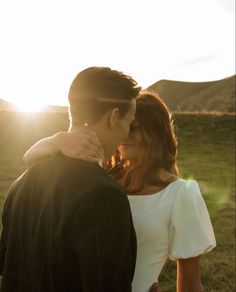 a man and woman standing next to each other in a field with the sun behind them