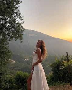 a woman in a white dress is standing on a hill with her legs spread out