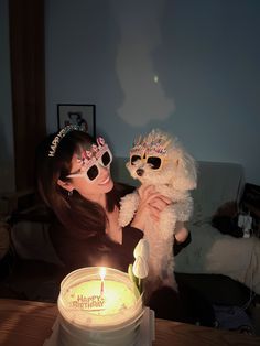 a woman holding a white dog in front of a birthday cake with candles on it