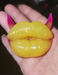 a hand holding a yellow and pink lip shaped toy in it's left palm