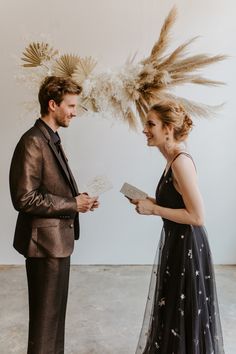 a man and woman standing next to each other in front of a white wall with feathers on it