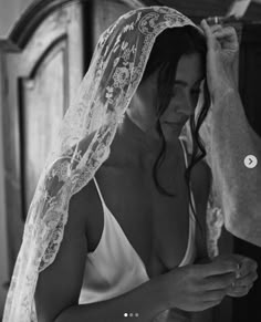 a woman wearing a wedding veil is looking at her cell phone while the man fixes it