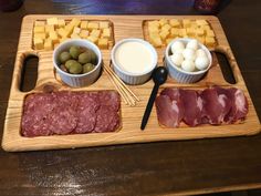 an assortment of meats, cheese and olives on a wooden tray with utensils