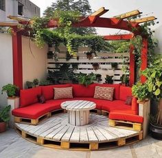 a red couch sitting on top of a wooden bench next to a white table and potted plants