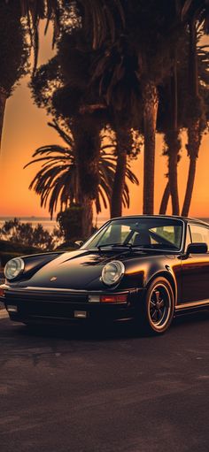 a black porsche parked in front of palm trees at sunset with the sun going down