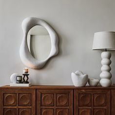 a white sculpture sitting on top of a wooden dresser next to a lamp and mirror