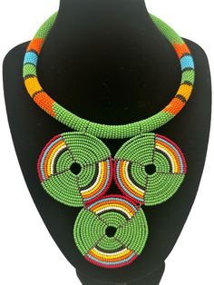 This stunning African necklace showcases a beautiful green beaded disc pendant that is truly authentic. The pendant is handcrafted and features intricate beading detail that is sure to impress. The necklace is perfect for those who appreciate the fine craftsmanship and unique jewellery. The beaded pendant is eye-catching and adds a touch of elegance to any outfit.  The diameter of the pendant - 5 inches. Neck Width - 16 inches. Traditional Green Hand-strung Beaded Necklaces, Traditional Green Hand-strung Necklaces, Traditional Green Adjustable Necklace, Adjustable Green Artisan Jewelry, Traditional Green Hand-strung Necklace, Green Adjustable Artisan Jewelry, Artisan Adjustable Green Jewelry, Green Handmade Traditional Necklaces, Traditional Green Hand-strung Jewelry