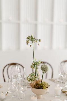 a white table topped with a vase filled with flowers and greenery next to candles