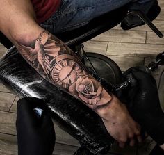 a man with a clock and roses tattoo on his arm is sitting in a chair