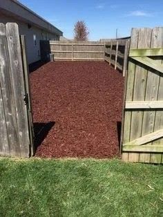 a fenced in area with grass and dirt on the ground next to an open wooden gate