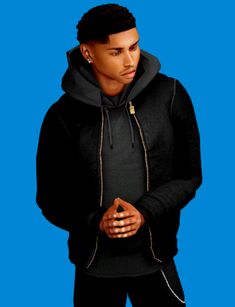 a man in a black hoodie is standing with his hands together