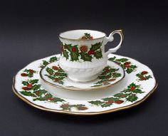 a white cup and saucer with holly designs on the rim, sitting on a black surface