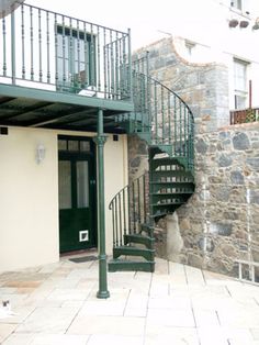 a spiral staircase in front of a building with stone walls and green metal railings