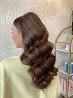 a woman with long brown hair is sitting in front of a shelf and she has her back turned to the camera