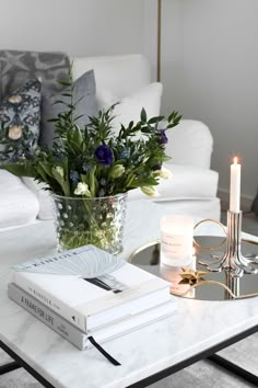 a coffee table with flowers and books on it in front of a white couches