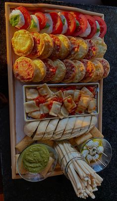 an assortment of food is displayed on a wooden tray with dipping sauces and bread sticks