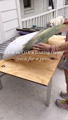 a woman holding a surfboard on top of a wooden table next to a dog