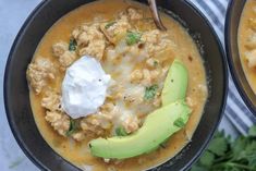 two black bowls filled with soup and topped with sour cream, avocado and tortilla chips