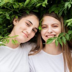 two young women standing next to each other in front of green leaves