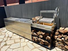 an outdoor grill with firewood stacked on the side and a brick wall behind it