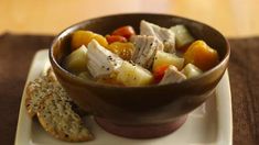 a bowl filled with meat and vegetables on top of a plate next to crackers