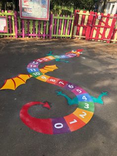 a colorful dragon painted on the ground in front of a fence with numbers and colors