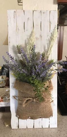 a burlap bag with flowers in it sitting on the floor next to a wooden sign