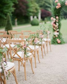 rows of chairs with flowers on them in front of an outdoor wedding ceremony arch at the end of a gravel path