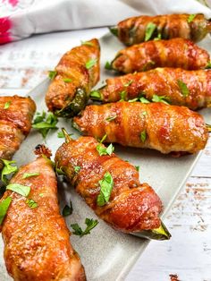 several pieces of meat wrapped in bacon and garnished with parsley on a white platter