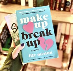 a person holding up a book that says make up break up in front of bookshelves