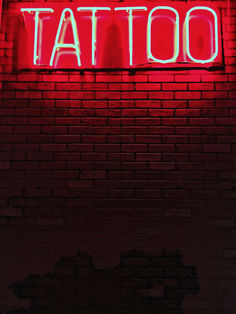 a red neon sign that says tattoo on a brick wall