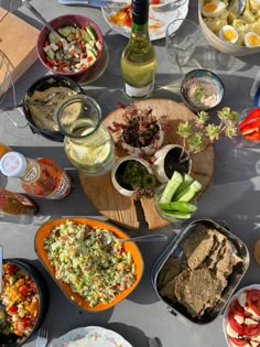 a table filled with plates and bowls of food next to bottles of wine on top of it