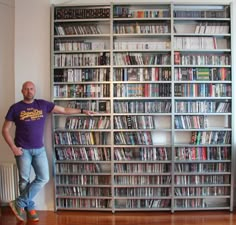 a man standing in front of a large book shelf filled with movies and video games