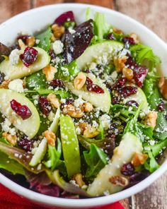 a salad with pears, cranberries and nuts in a white bowl on a wooden table