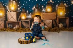 a baby boy sitting on the floor eating cake in front of a backdrop with lights