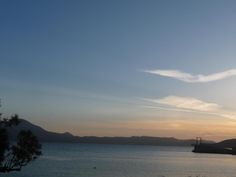 the sun is setting over water with mountains in the background