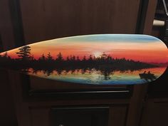 a painted surfboard sitting on top of a wooden cabinet next to a door with a boat in the water