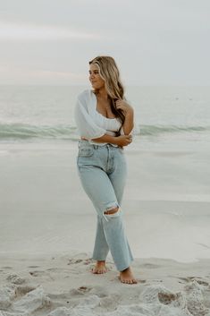 a woman standing on top of a sandy beach next to the ocean with her arms crossed