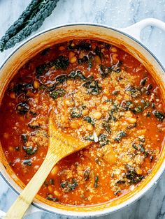 a pot filled with stew and vegetables on top of a marble counter next to a wooden spoon