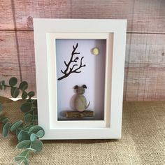 a shadow box frame with a small stuffed animal in it and some leaves on the table