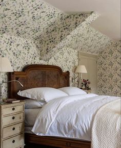 a bedroom with floral wallpaper and white linens on the bed, along with two nightstands