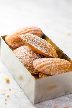 powdered sugar covered doughnuts in a metal container on a white countertop