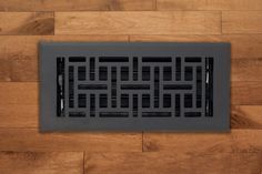 a floor vent cover on the side of a wooden floor with black grates in it