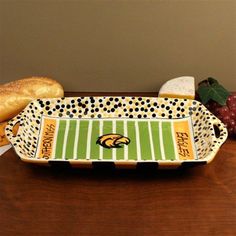 a green and white tray with some bread in it on a table next to grapes