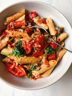 a white bowl filled with pasta covered in tomato sauce and spinach on top of a table