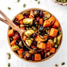 a bowl filled with sweet potatoes, pumpkins and cranberry sauce next to two wooden spoons